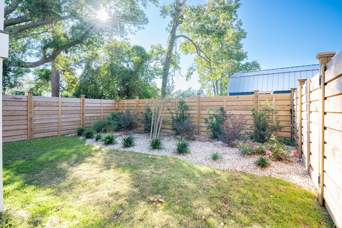 A beautifully landscaped backyard enclosed by a wooden fence, with sunlight filtering through lush trees and ample green space for play. The area is inviting and peaceful, suggesting a safe, private haven perfectly suited to both pets and children.