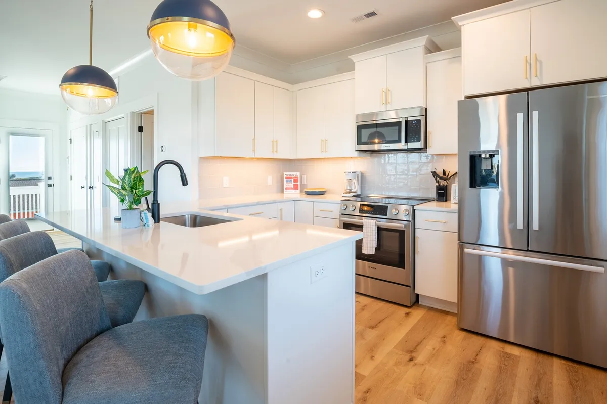 A modern kitchen with an island countertop, stainless steel Bosch appliances, elegant light fixtures, and stylish cabinetry. The kitchen is designed for both cooking and socializing, with plenty of seating around the island and open sightlines to the rest of the main floor.