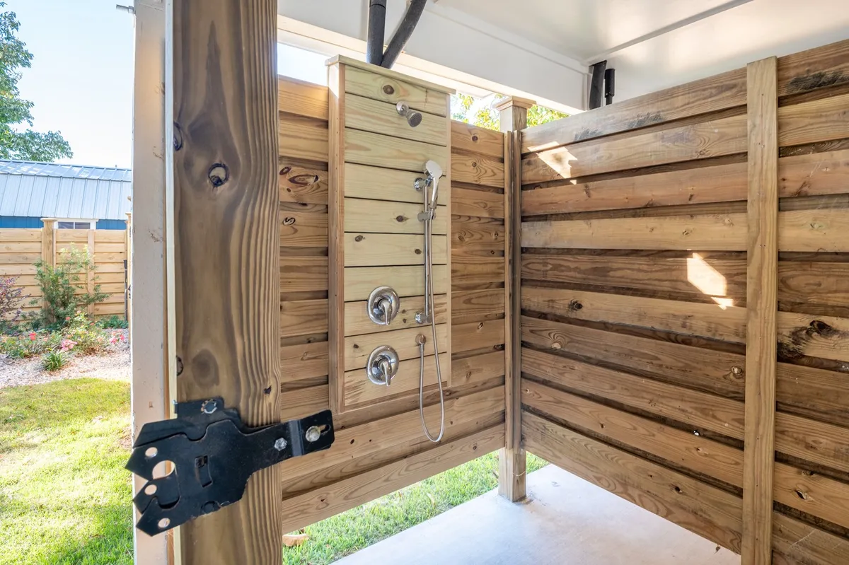 A dedicated outdoor shower with wooden panels and a sturdy door, located in a sunny part of the yard. The design is practical and welcoming, making it ideal for rinsing off after sandy beach adventures or playtime in the yard.