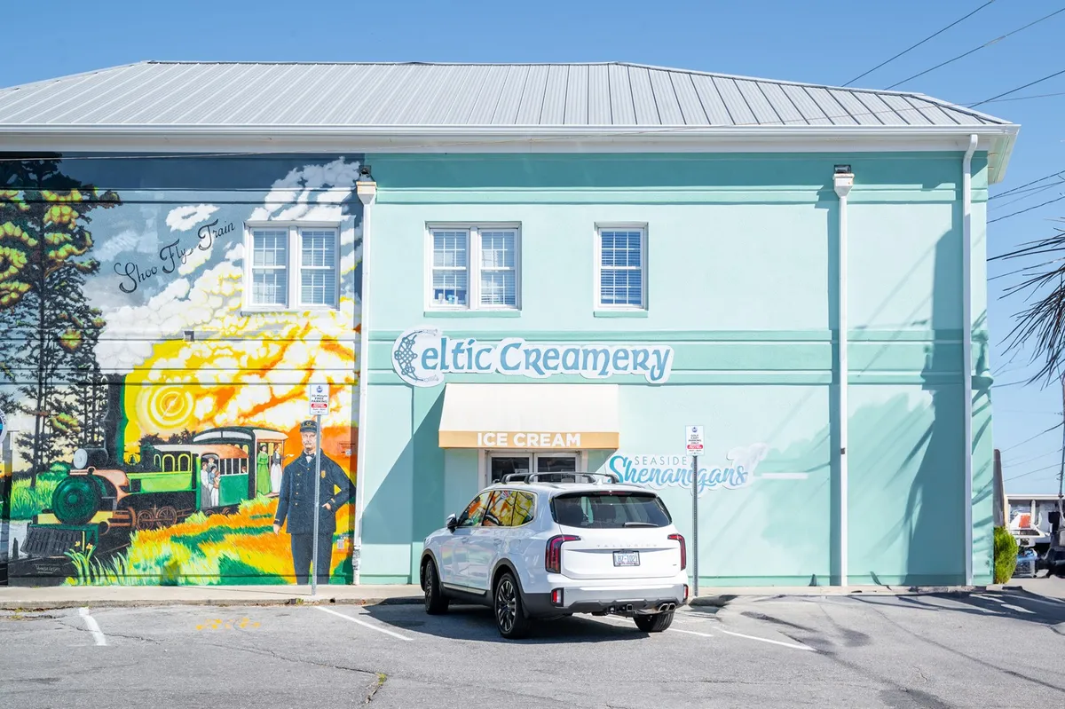 The exterior of Celtic Creamery, a beloved ice cream shop, complete with a colorful mural and inviting outdoor seating. The sunny atmosphere and playful signage encourage guests to stop in for a sweet treat and snap photos with family.