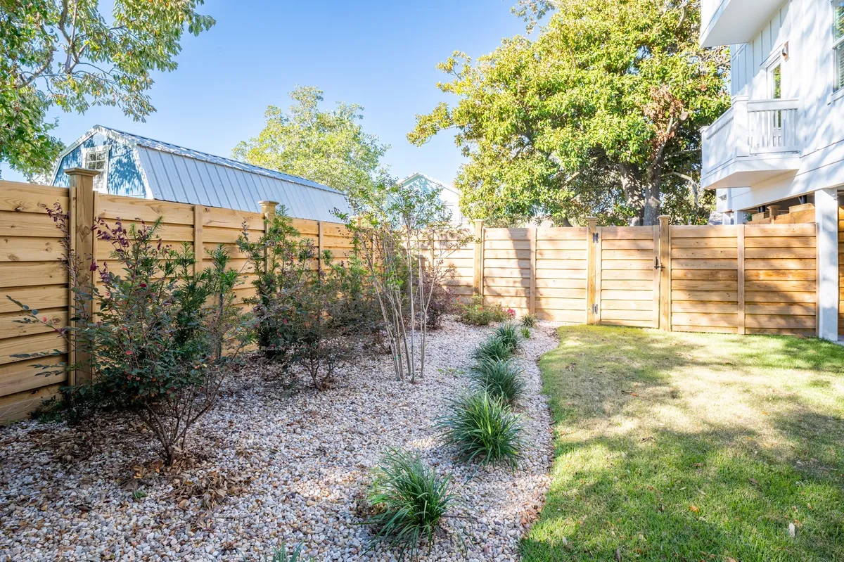 A peaceful, fenced backyard with lush greenery, a gravel pathway, and wooden fencing. The area is private and spacious—ideal for letting dogs play or relaxing after a day at the beach.