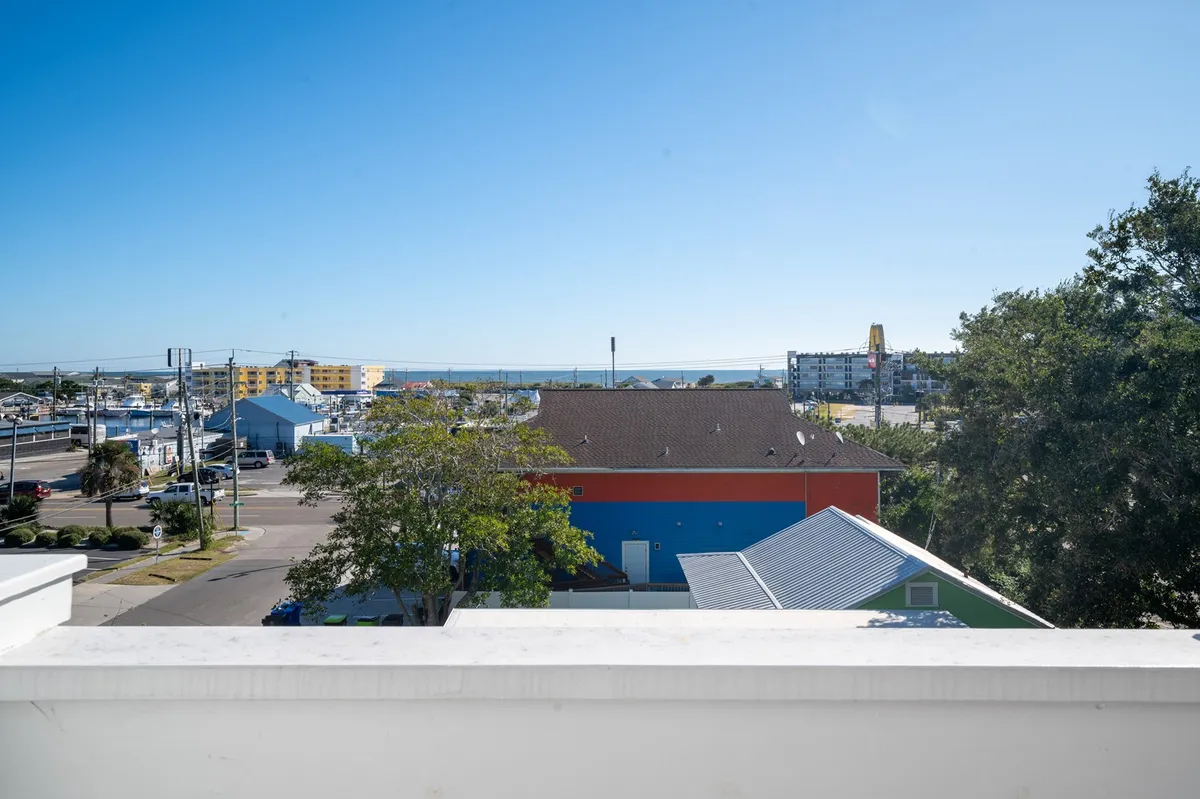 A cheerful coastal view showcasing the ocean, colorful local buildings, and vibrant surroundings. The scene includes a tree in the foreground and expansive water, capturing the lively atmosphere of Carolina Beach.