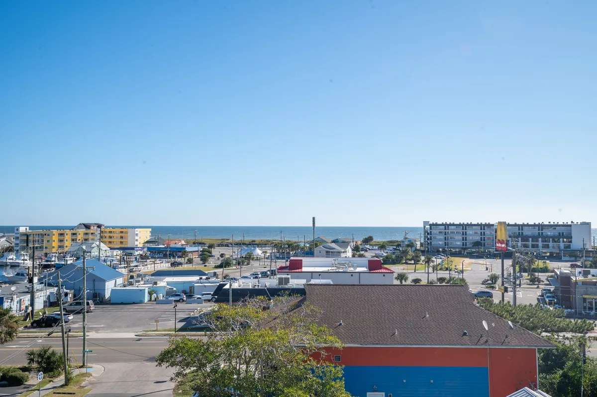 A panoramic view of the ocean, marina, and bustling beachfront with colorful buildings and a clear blue sky. The lively scene suggests easy strolls to waterfront dining, shopping, and recreation.