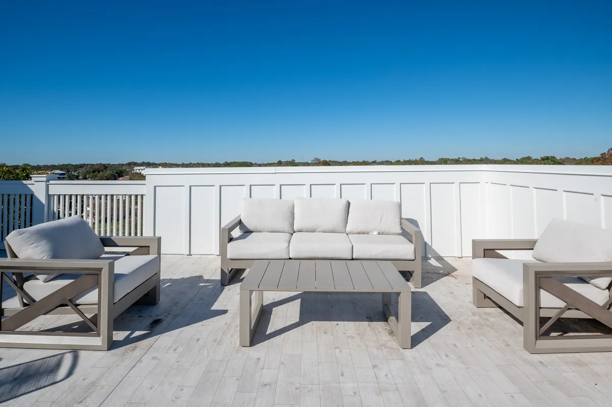 An inviting exterior seating area set behind a white fence under an open blue sky. The space encourages relaxation and socialization, with a tranquil atmosphere that highlights the enjoyment of outdoor living.